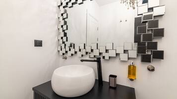Une salle de bain moderne avec un lavabo blanc, un robinet noir et un miroir orné d’un motif géométrique.