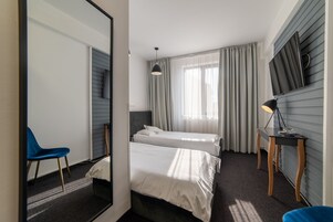 Habitación de hotel con dos camas, un escritorio, una silla y un televisor montado en la pared.