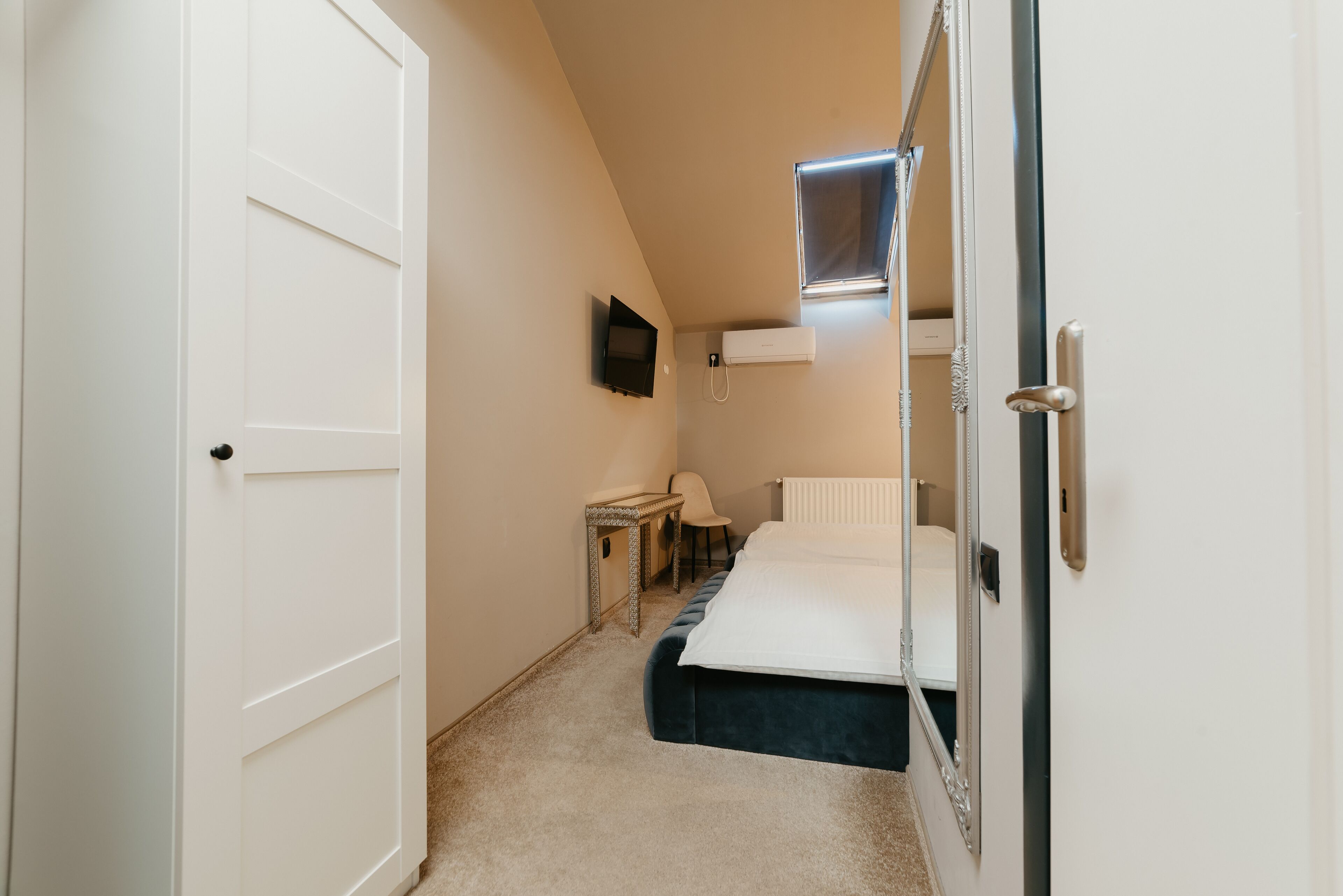 Ein Zimmer mit einem Bett, einem kleinen Tisch, einem Sessel, einem Fernseher und einem Fenster mit einer Lampe.
