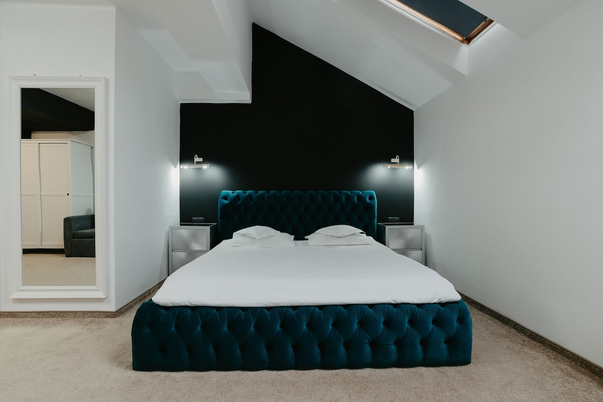 A bedroom with a large bed, white bedding, and a dark headboard. There are two bedside tables with lamps.