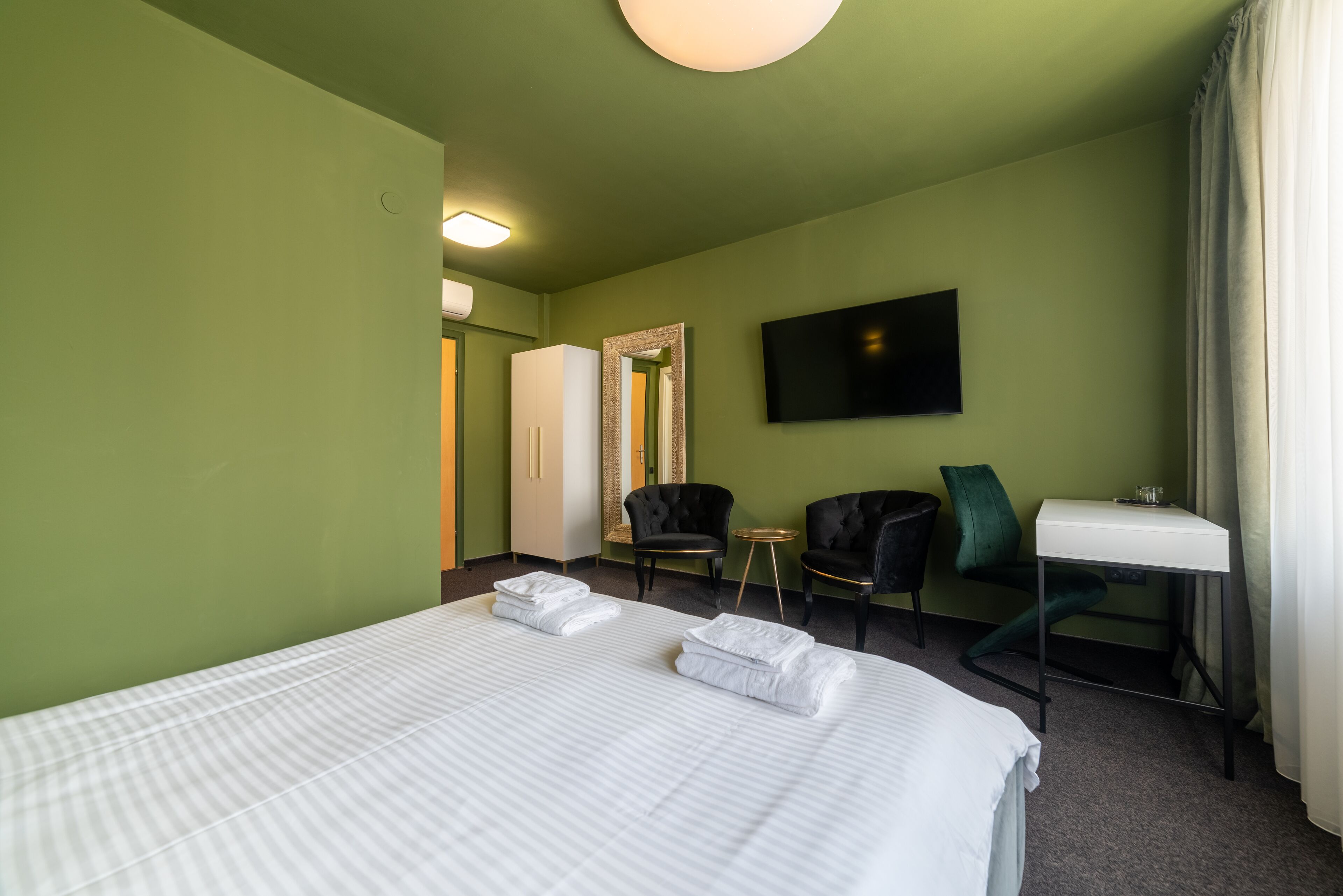 Una habitación de hotel con una cama grande, dos sillas, una mesita, un televisor y un espejo.