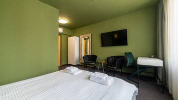 A hotel room with a large bed, two chairs, a small table, a TV, and a mirror.
