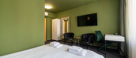 Una habitación de hotel con una cama grande, dos sillas, una mesita, un televisor y un espejo.
