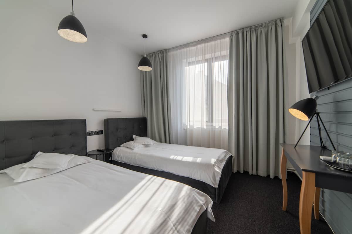 A hotel room with two beds, a desk, a TV, and a large window with curtains.