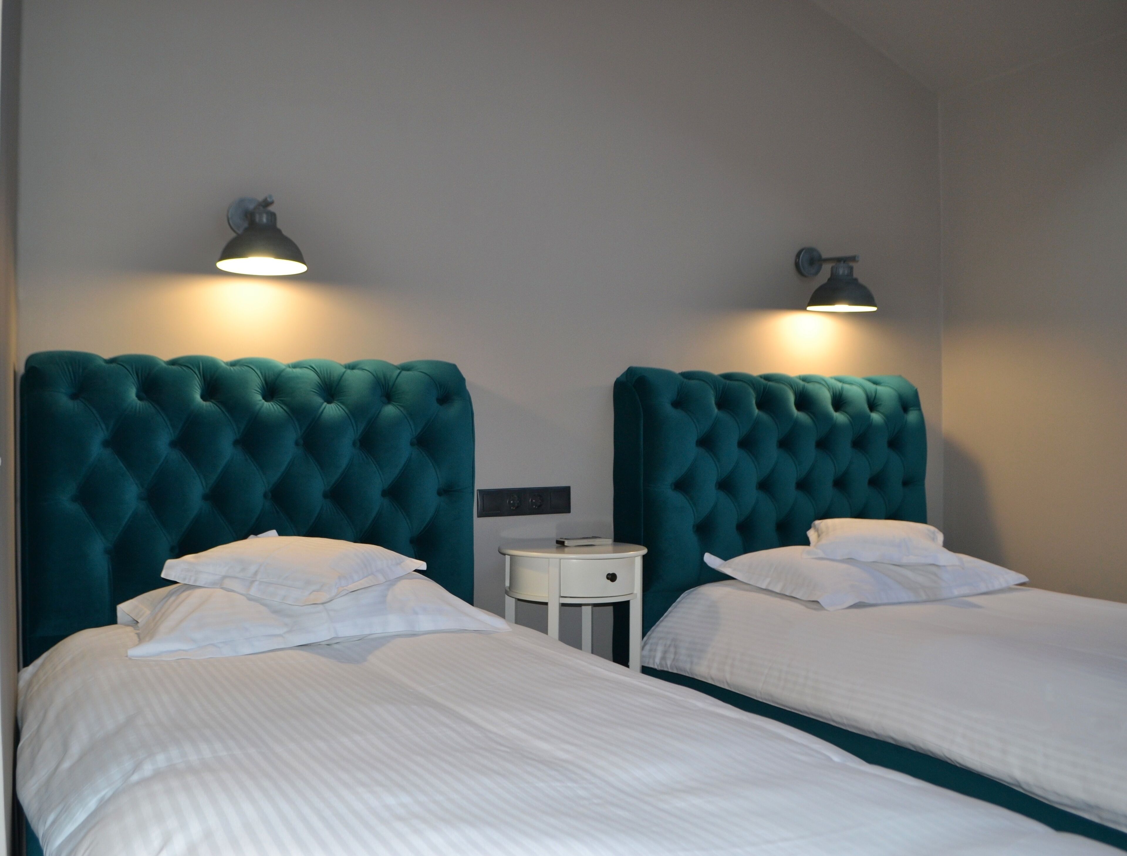 A hotel room with two beds, each with a teal headboard and white bedding. There are two bedside tables with lamps.