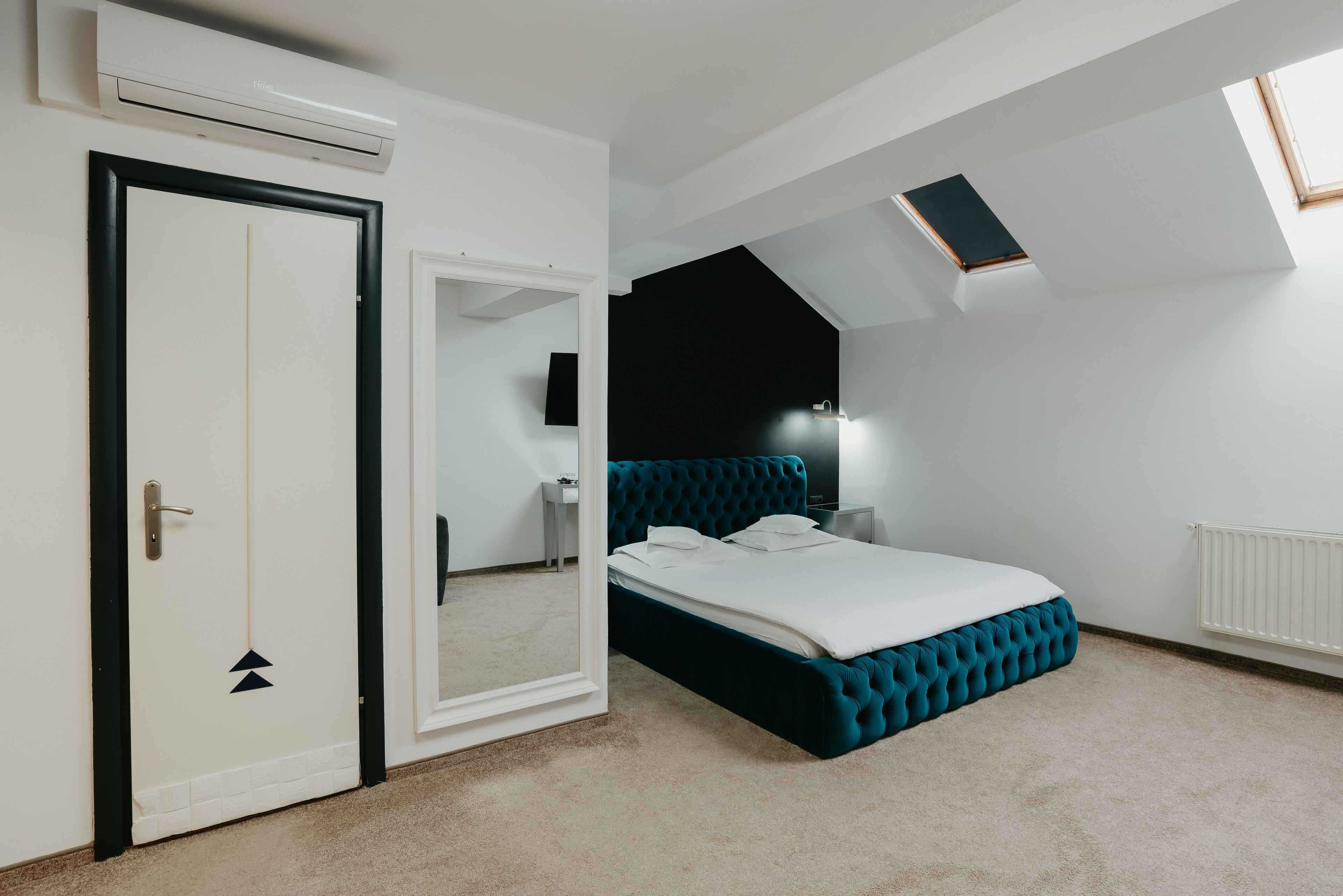 Een slaapkamer met een bed, een deur, een spiegel, een nachtkastje, een lamp en een raam.