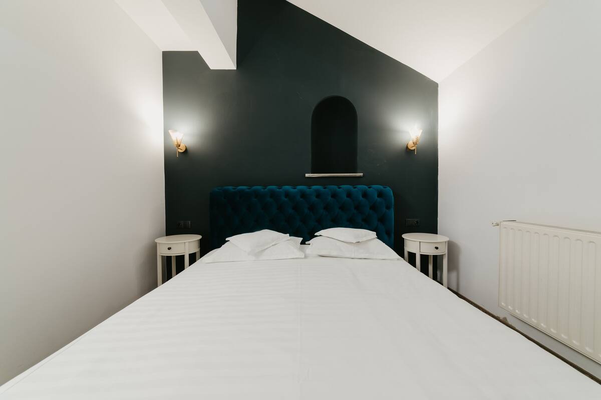 A bedroom with a large bed, two bedside tables, a dark headboard, and two wall-mounted lights.