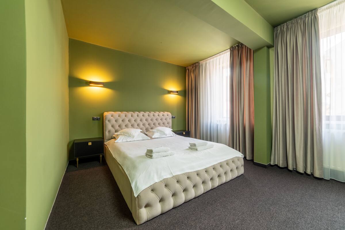 A neatly made bed with a tufted headboard, two bedside tables, and a radiator.
