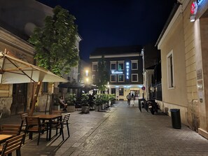 A hotel with a sign reading "HOTEL" and "Fullerton" in illuminated letters. There are outdoor tables and chairs, and a few people walking in the street.