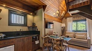 A cozy kitchen with wooden cabinets, a dining table with chairs, a sofa, and a TV. - Hotel Fioreze Chalés (Gramado)