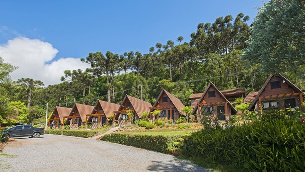 A row of wooden cabins with pitched roofs, surrounded by lush greenery and trees. - Hotel Fioreze Chalés (Gramado)