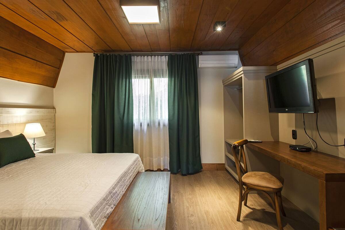 A hotel room with a bed, a desk with a chair, a television, and a window with curtains.