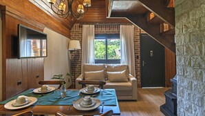 A cozy dining area with a wooden table set for two, a sofa, and a fireplace. - Hotel Fioreze Chalés (Gramado)