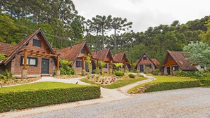 A row of log cabin-style cottages with pitched roofs, surrounded by lush greenery and tall trees. - Hotel Fioreze Chalés (Gramado)