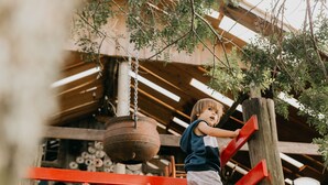 A child climbing a wooden structure with red supports. - Hotel Fioreze Chalés (Gramado)