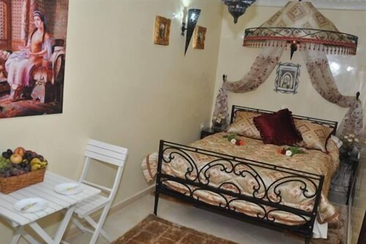 A bedroom with a bed, a white chair, a fruit basket, and a decorative canopy.