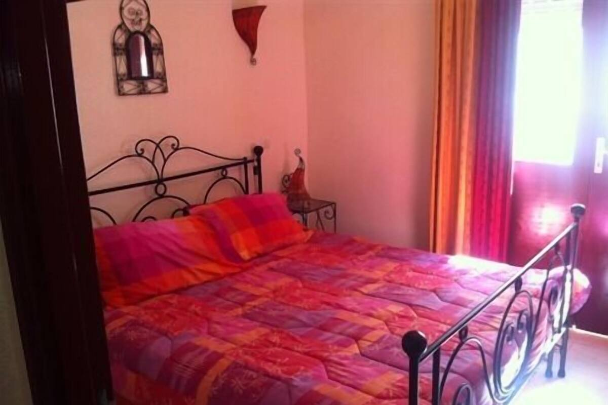 A bedroom with a bed, a nightstand, a wall clock, and a window with curtains.