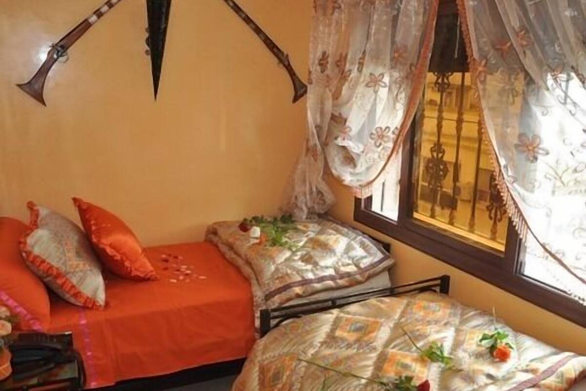 A cozy bedroom with two beds, one with orange bedding and the other with patterned bedding.