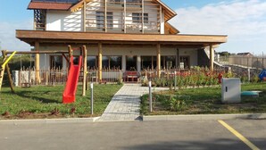 Ein zweistöckiges Gebäude mit einem geneigten Dach, einer überdachten Veranda und einem Spielbereich mit einer roten Rutsche.