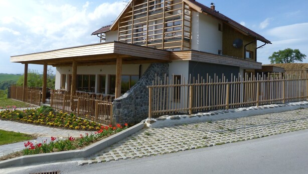 Ein modernes Haus mit Satteldach, Holzbalkon, Steinwand und einem umzäunten Garten.