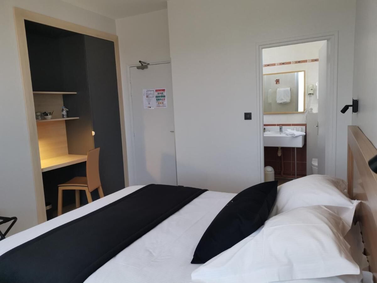 Habitación de hotel con cama, escritorio y baño visible a través de una puerta abierta.
