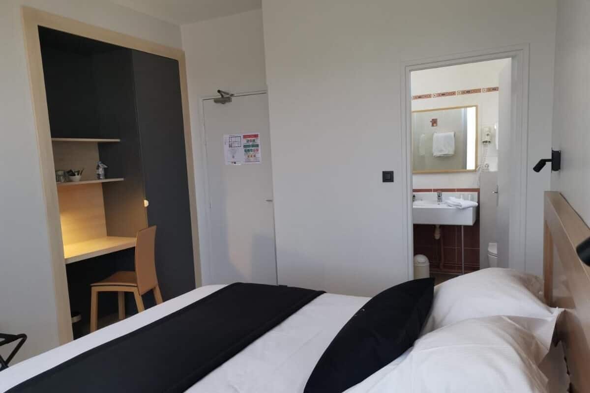 Une chambre d’hôtel avec un lit, un bureau et une salle de bain, visibles à travers une porte ouverte.