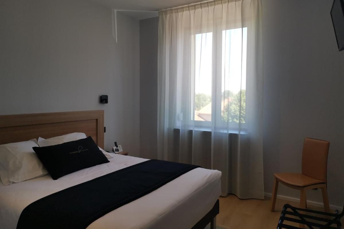 Een hotelkamer met een bed, een stoel, een raam met gordijnen en uitzicht.