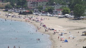 Una playa con gente nadando y tomando el sol, tiendas de campaña y coches aparcados a lo largo de la orilla.