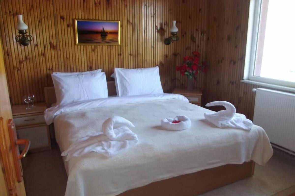 A neatly made bed with white linens, two pillows, and two swan-shaped towels on the bed.