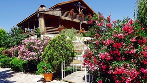 Un edificio de madera con balcón, rodeado de plantas en flor y follaje.