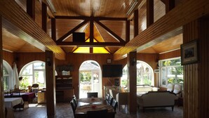 Una habitación amplia con techo de madera, un comedor con mesa y sillas, un sofá y un televisor montado en la pared.