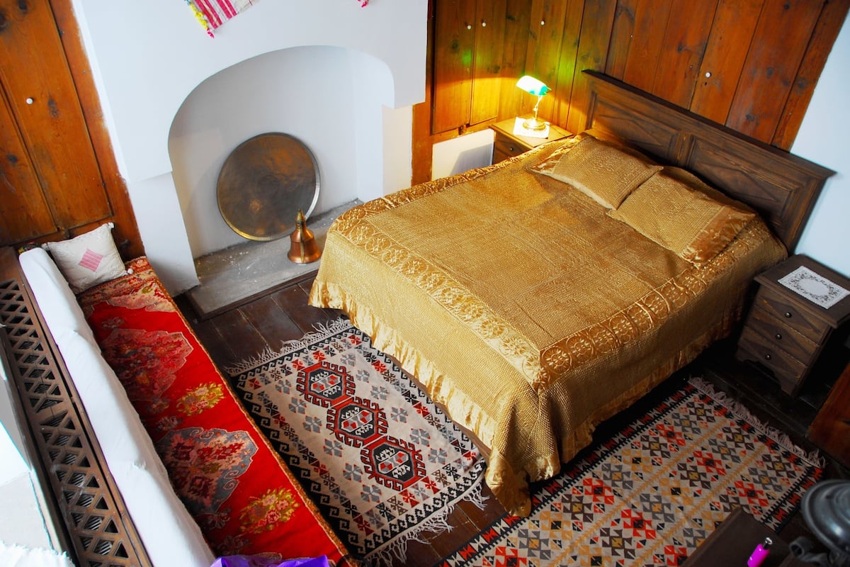 A traditional room with a bed, a wooden headboard, a nightstand, a lamp, and patterned rugs.