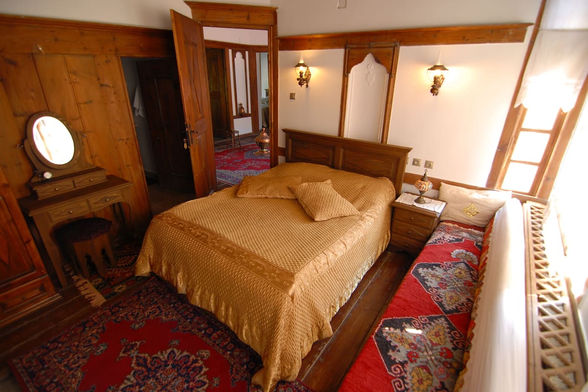 A traditional room with a wooden bed, a mirror, a nightstand, and a red patterned carpet.