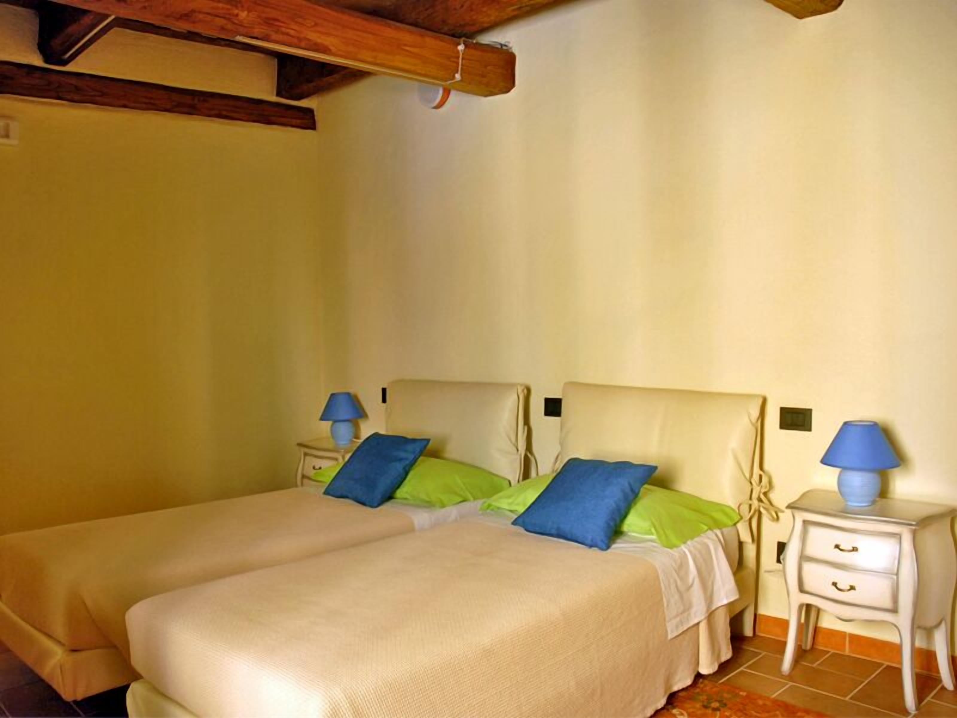 Un letto matrimoniale con due cuscini, un comodino con una lampada e un tavolino notte con una lampada.