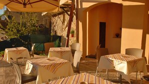 An outdoor patio with tables and chairs, covered by umbrellas, and surrounded by stone walls and greenery. - Thalassa Locanda B&B e Appartamento (Arcidosso)