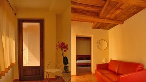 A room with a wooden ceiling, a red sofa, a small table with a vase of flowers, and a bed in the background. - Thalassa Locanda B&B e Appartamento (Arcidosso)