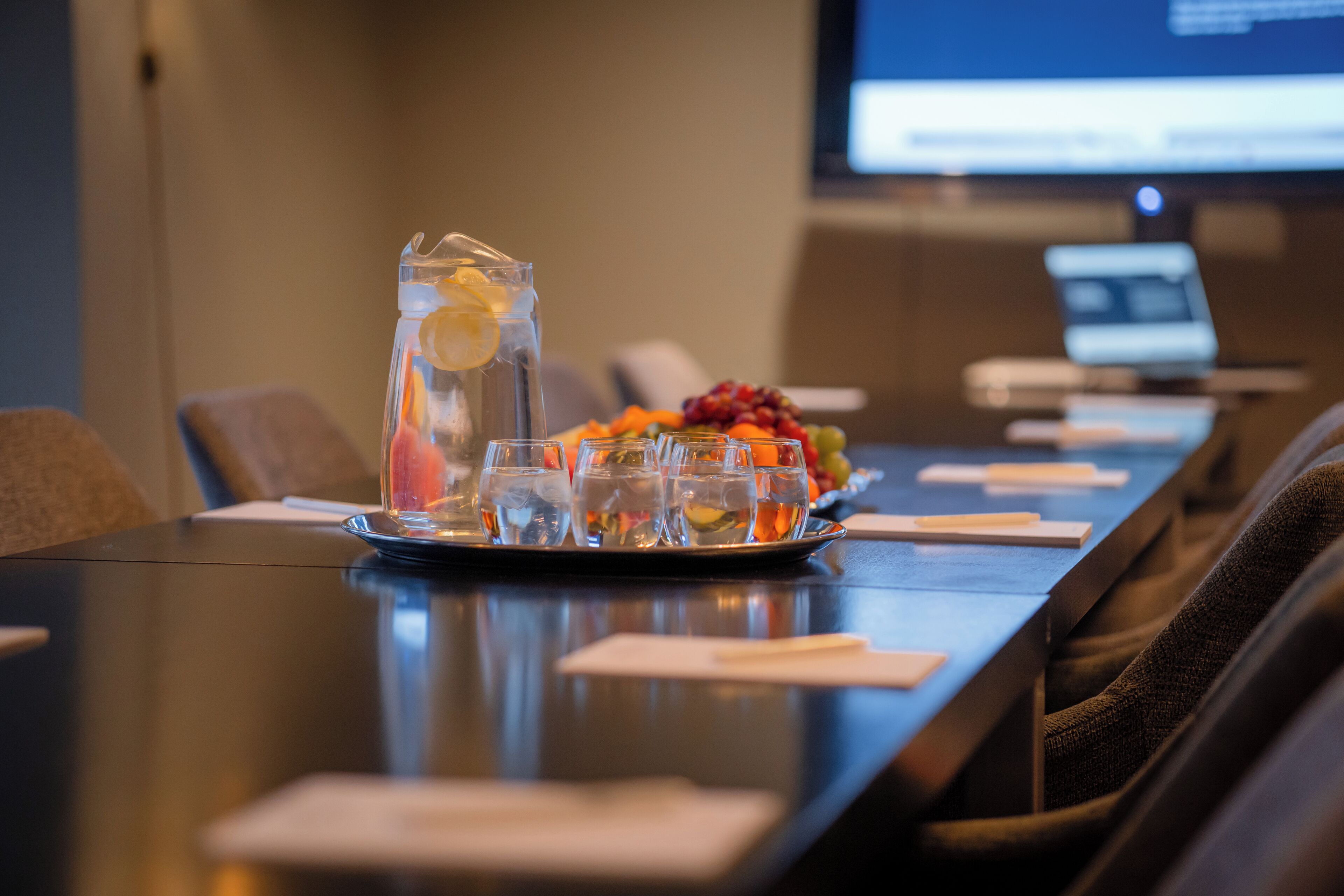 A conference table with a pitcher of water, glasses, and a fruit platter.