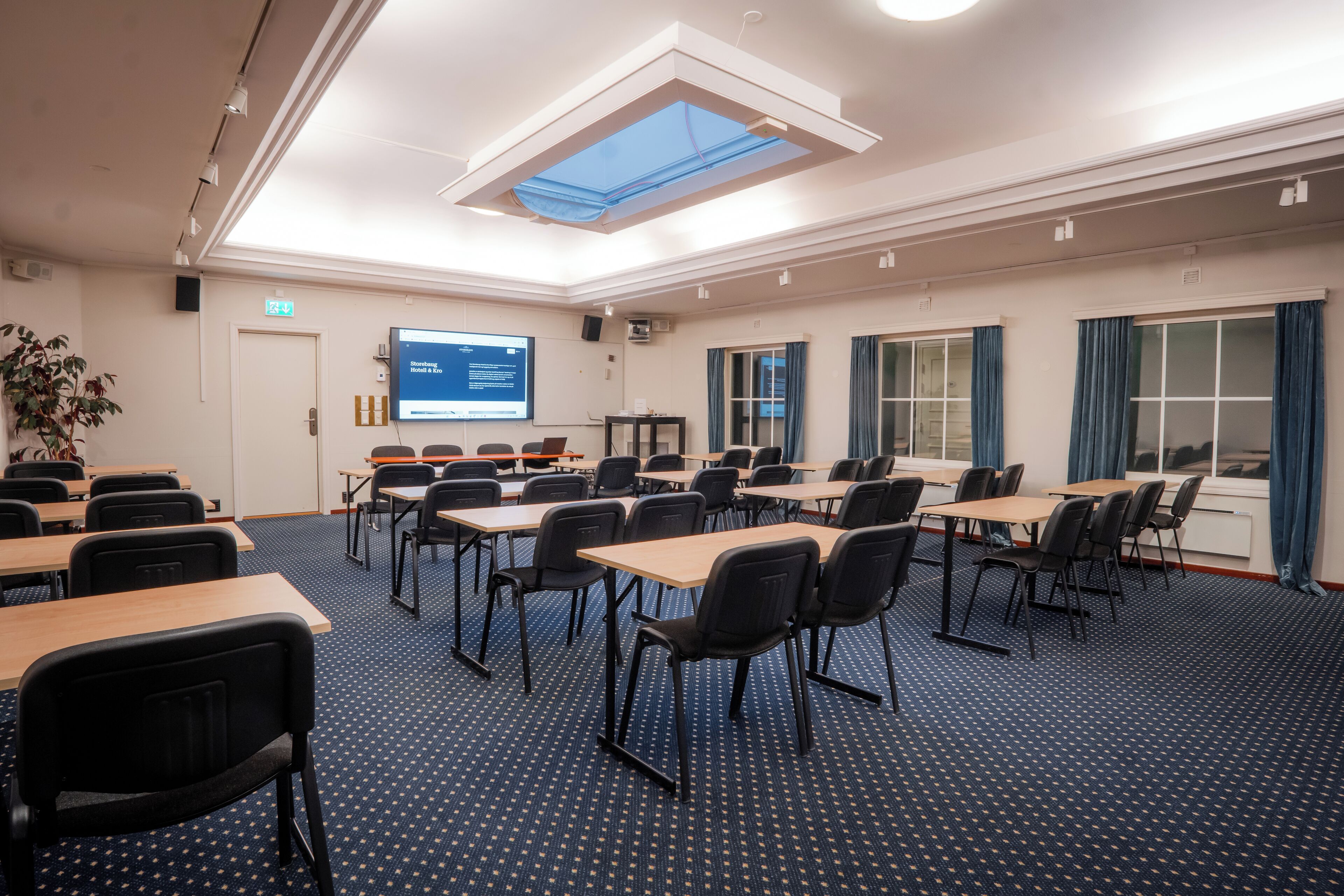 A conference room with tables and chairs, a projector screen, and a large window with curtains.
