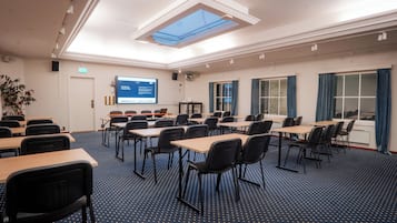 A conference room with tables and chairs, a projector screen, and a large window with curtains.