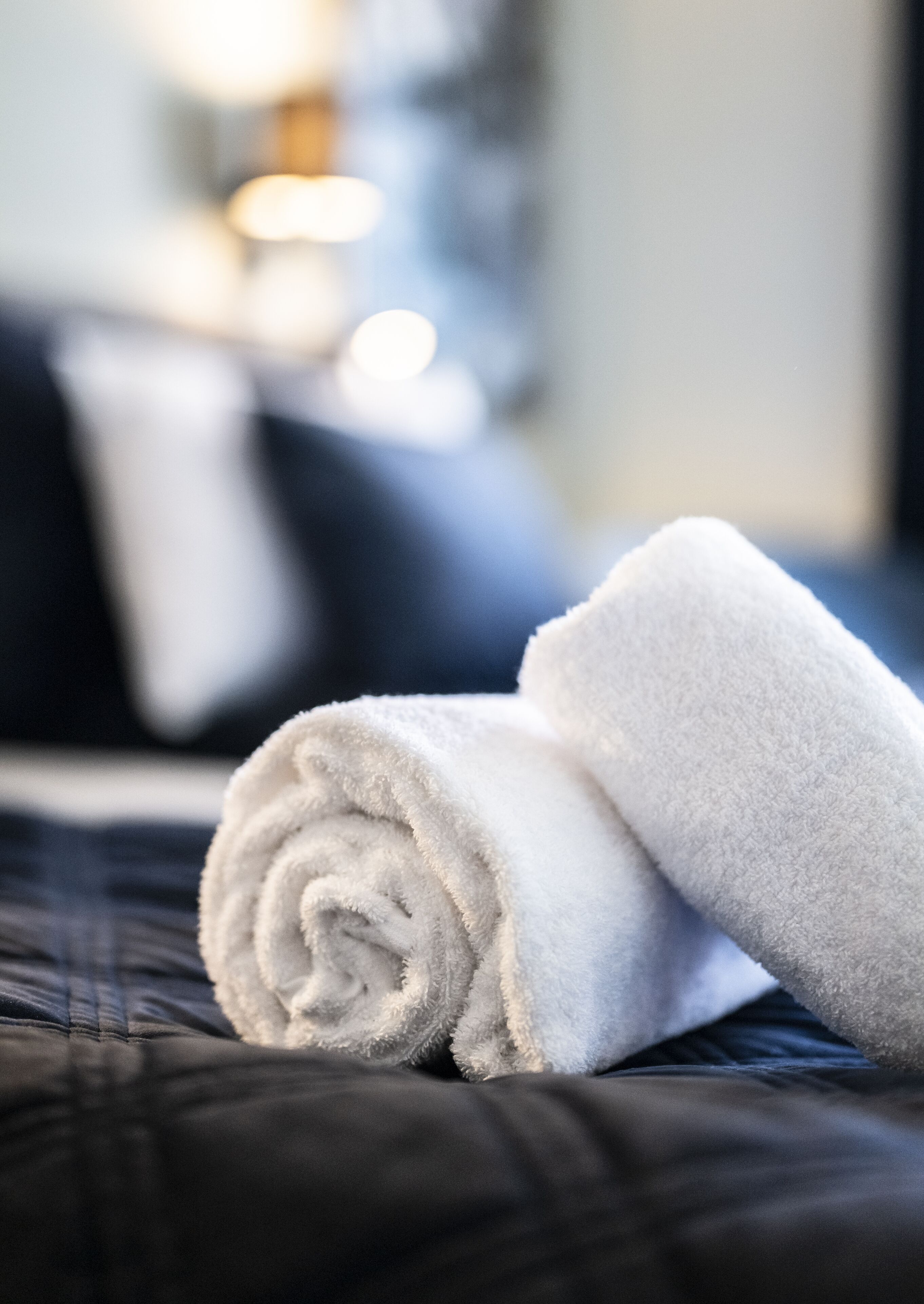 A neatly folded white towel on a dark-colored bed in a hotel room.