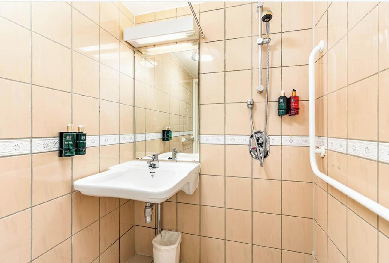 A bathroom with beige tiles, a white sink, a mirror, and a shower with a handheld showerhead.