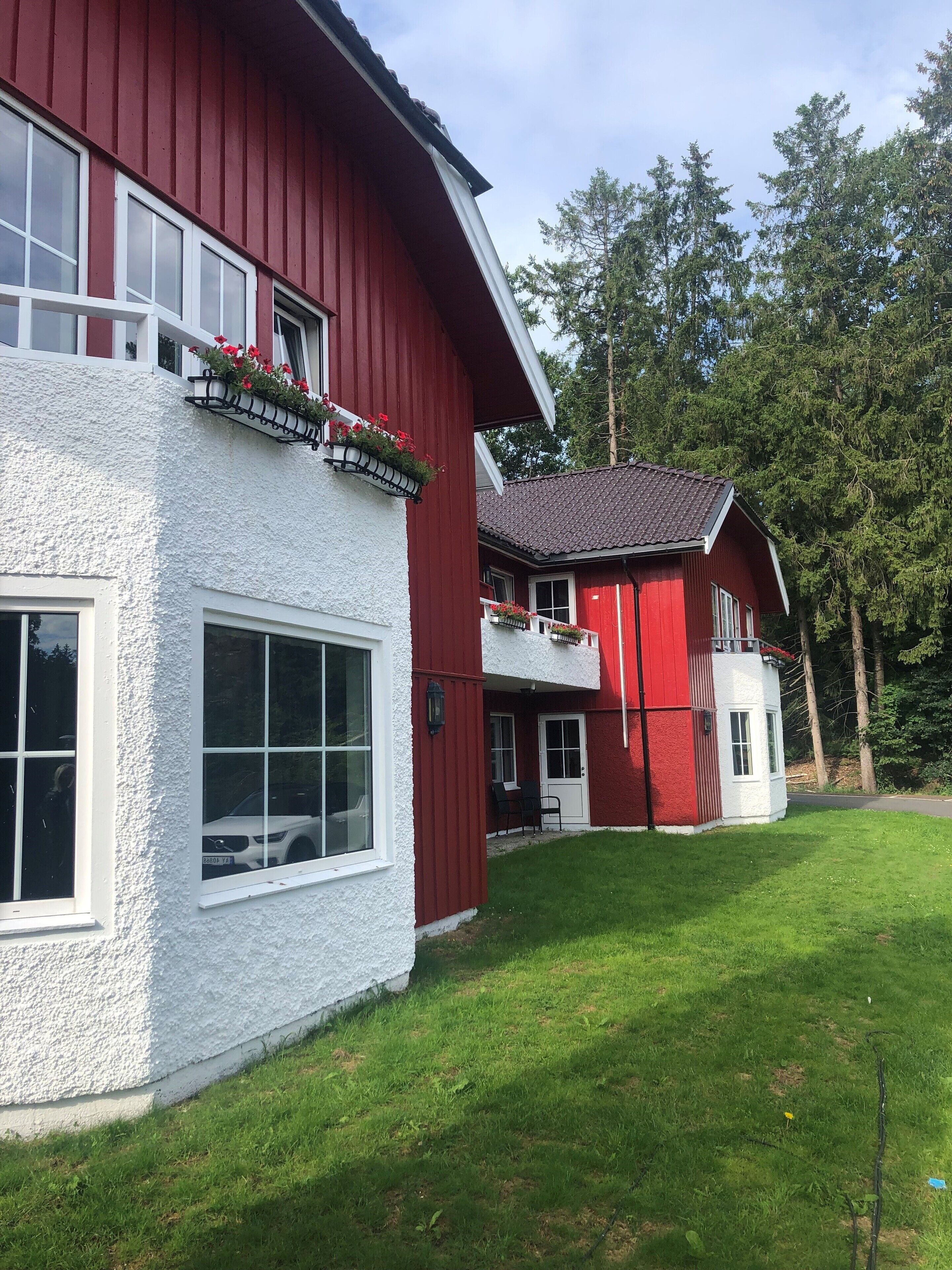 A red and white house with a balcony, a white exterior wall, and a green lawn.