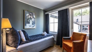 Une petite pièce comprenant un lit, une chaise, une lampe et une fenêtre avec des rideaux.