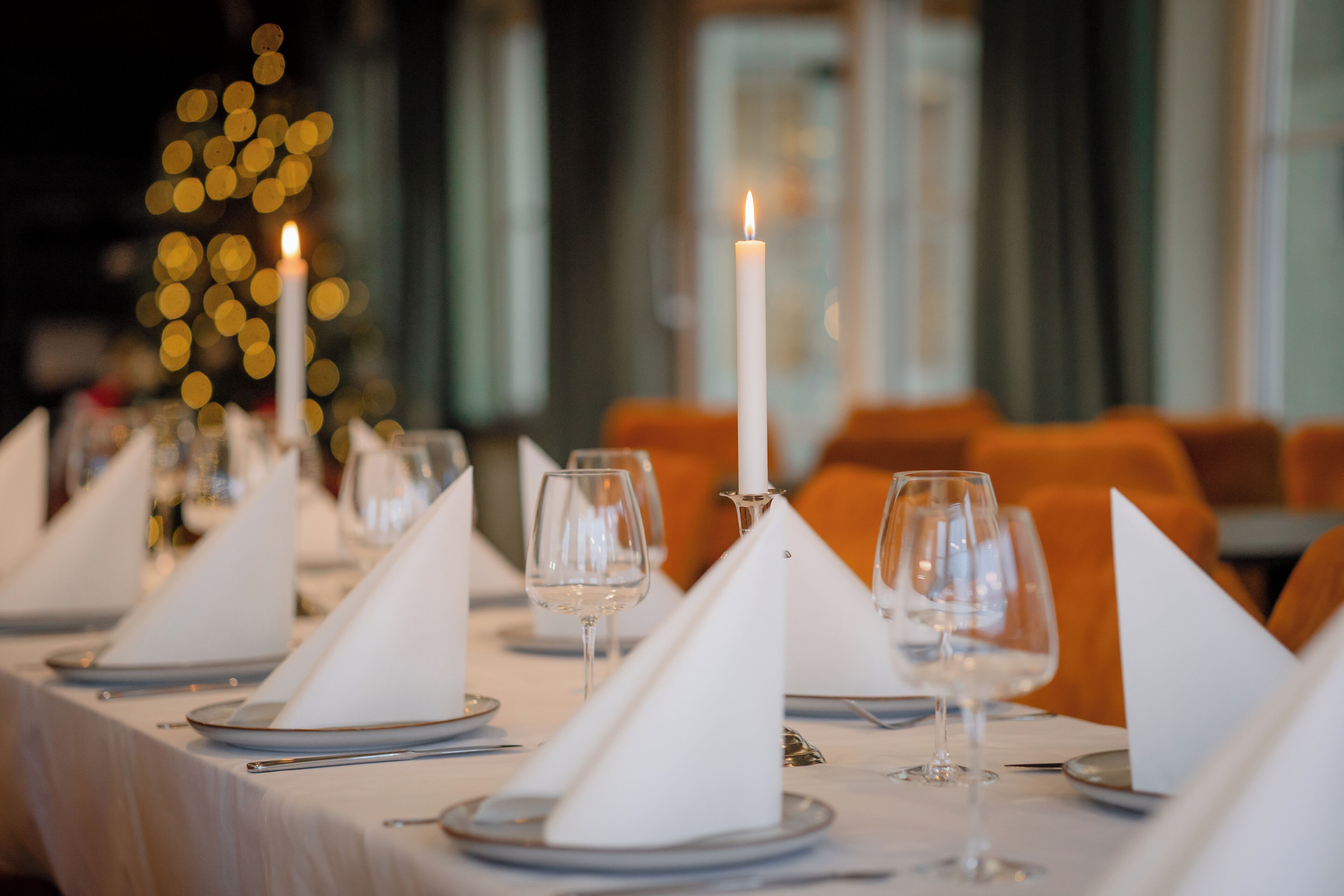 Juhlavaasti katettu ruokapöytä: valkoiset servetit, viinilasit ja sytytetty kynttilä.