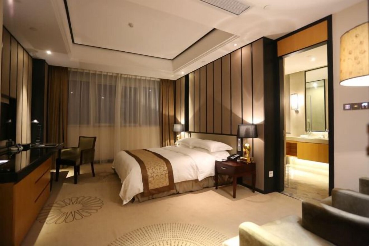 A hotel room with a bed, bedside table, lamp, chair, and a view of the bathroom.