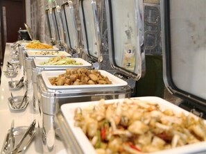 Un bufé con diversos platos en recipientes metálicos, utensilios y una copa.