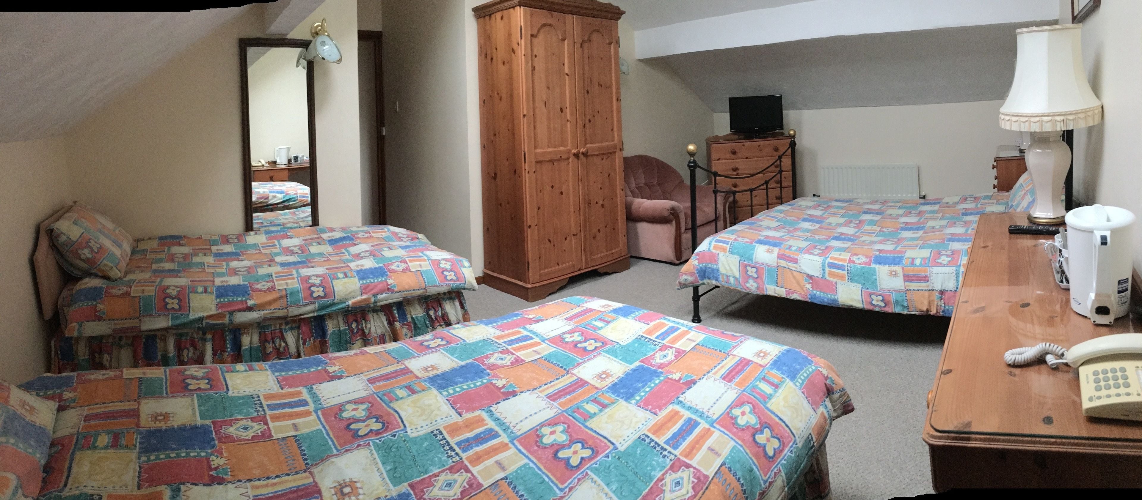 A bedroom with two beds, a wooden wardrobe, a desk with a lamp, and a telephone.