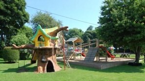 Un parque infantil con una casa del árbol, toboganes y mesas de picnic.