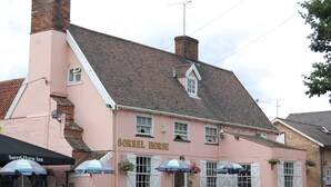 Un edificio rosa con el letrero "Sorrel Horse Inn" y mesas al aire libre cubiertas con sombrillas.