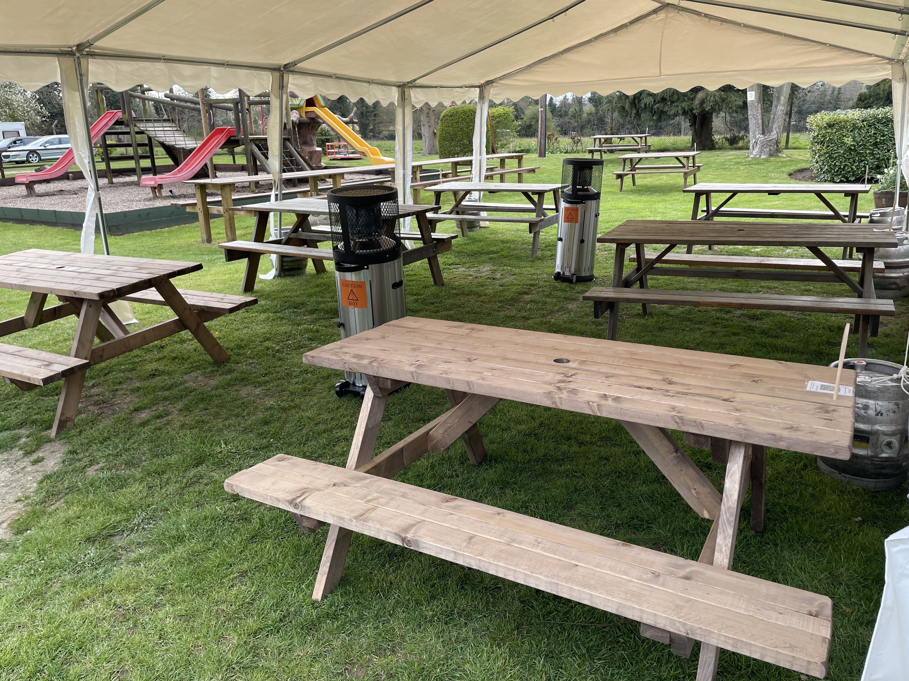 Un área de picnic con mesas y bancos de madera, un parque infantil con toboganes y una tienda de campaña que ofrece sombra.